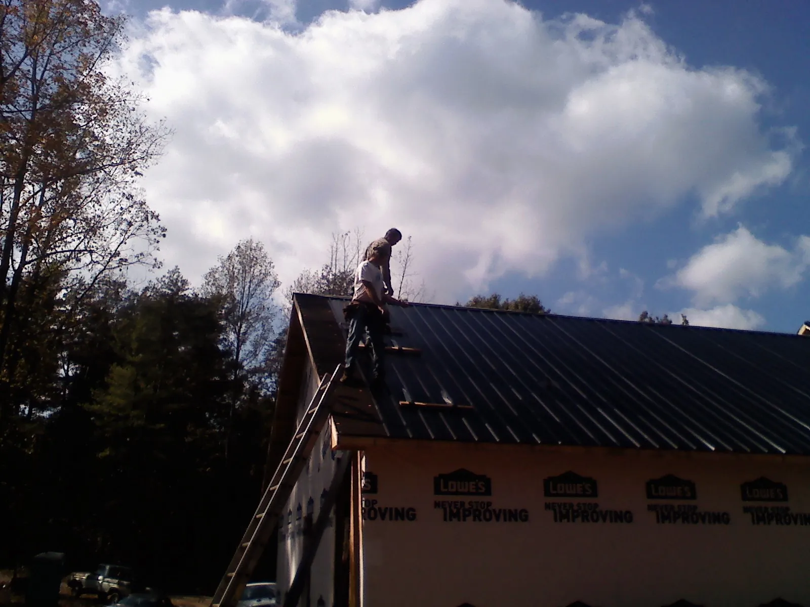 Roofer fastening dark metal panels high against a cloudy sky, from a Roof Inspection job in New Hartford